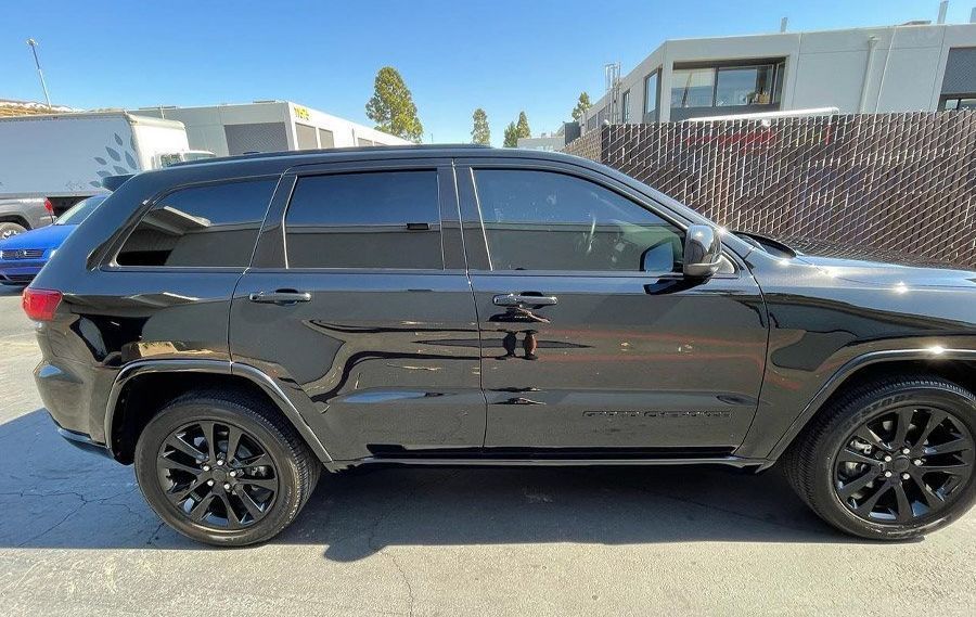 Black SUV parked in sunlight beside a chain-link fence and buildings