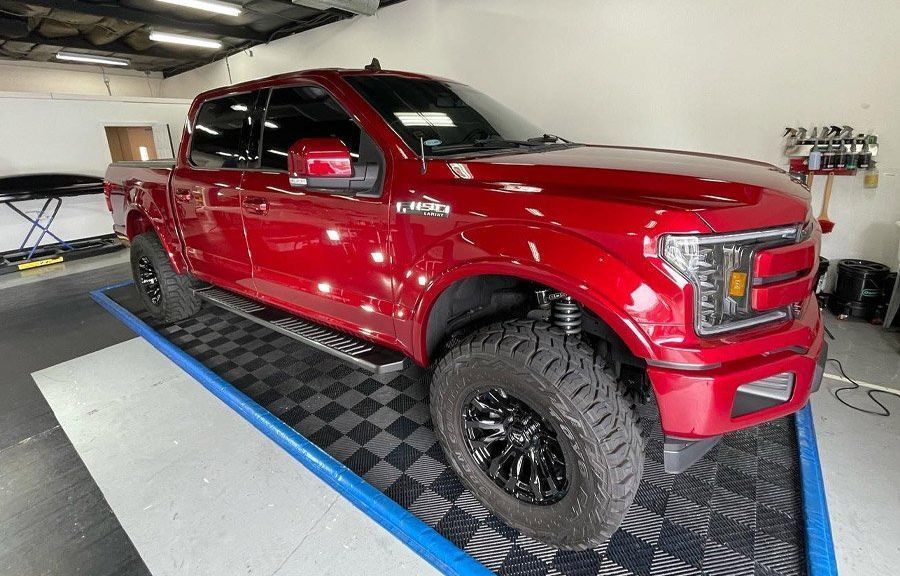 Red lifted pickup truck in a garage, shown on a blue-and-black platform.