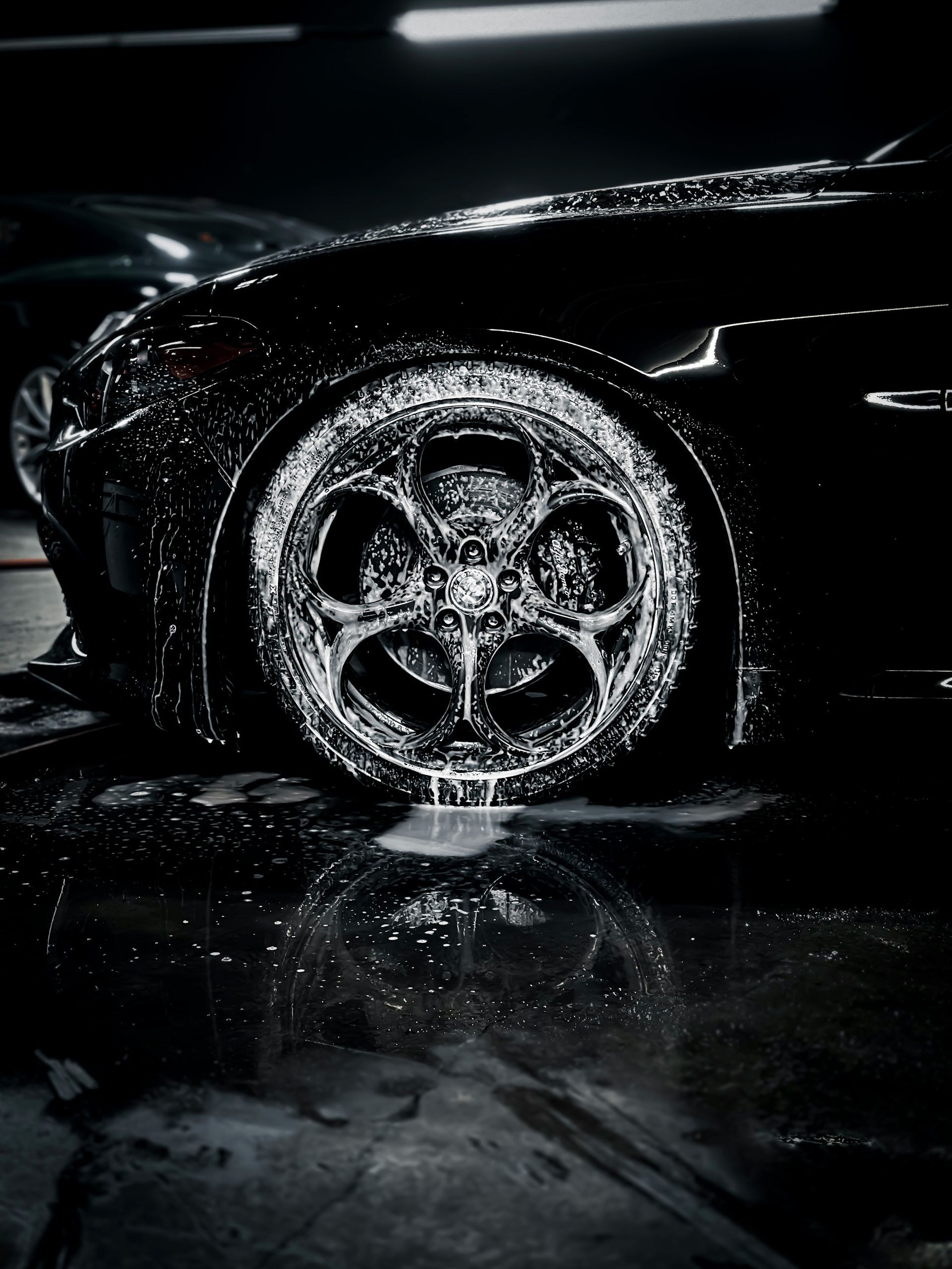 Close-up of a black car wheel splashed with water in a dark, reflective setting