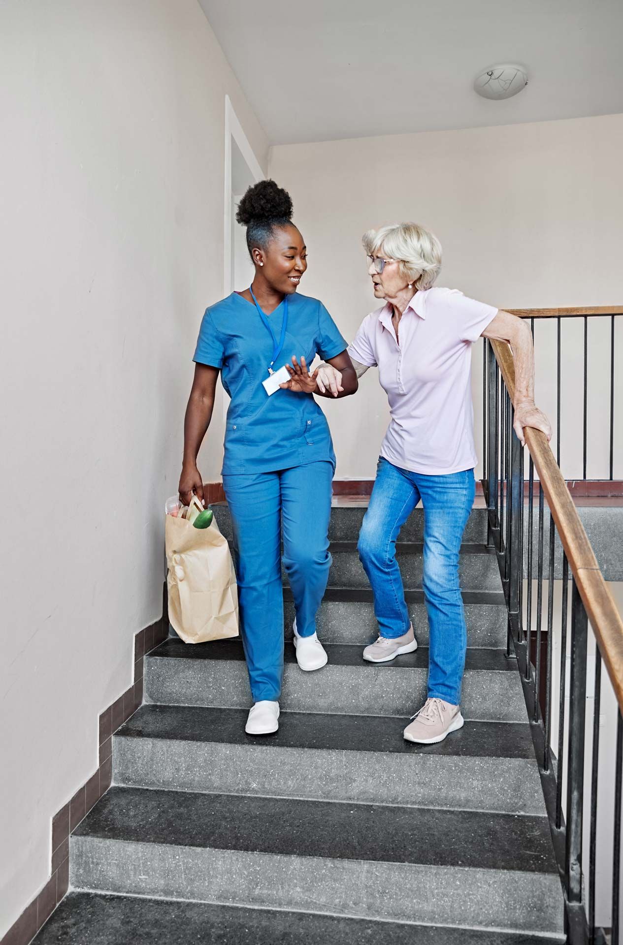 Woman helps senior woman descend stairs.
