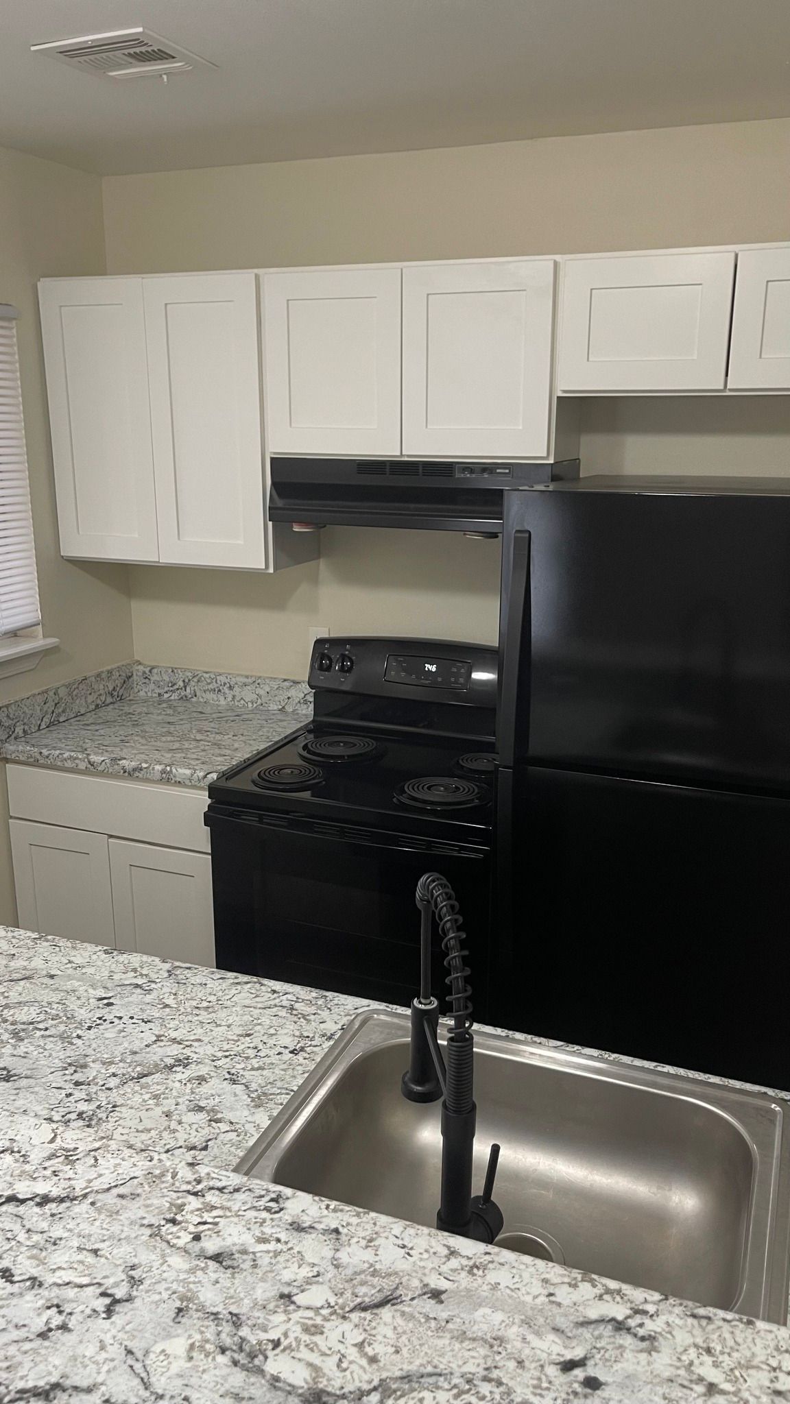 A kitchen with a black refrigerator , stove , sink and granite counter tops.