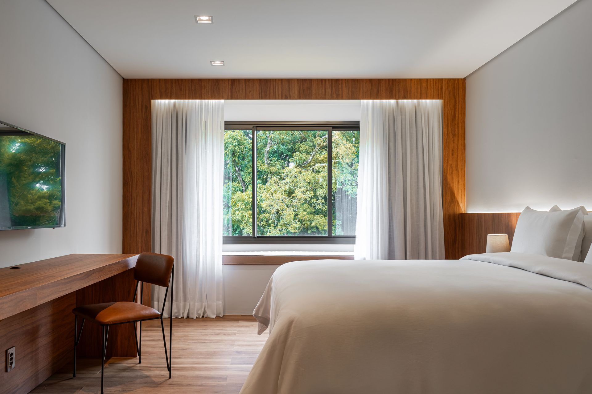 Um quarto de hotel com uma cama, cadeira, escrivaninha e televisão.