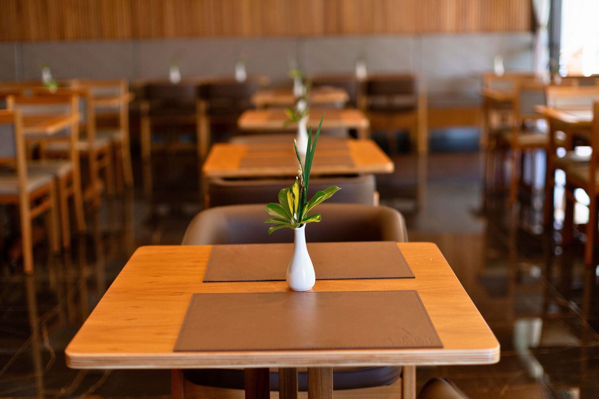 Um restaurante com mesas e cadeiras e um vaso de flores sobre a mesa.