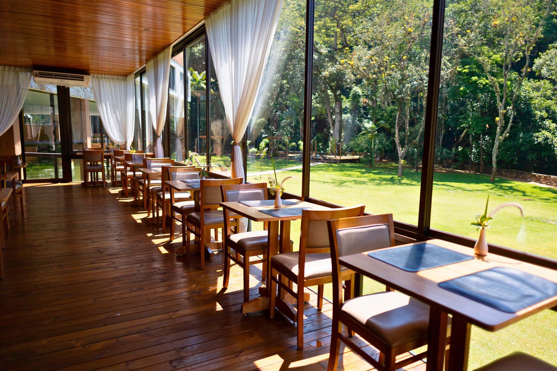 Um restaurante com mesas e cadeiras em frente a uma grande janela.