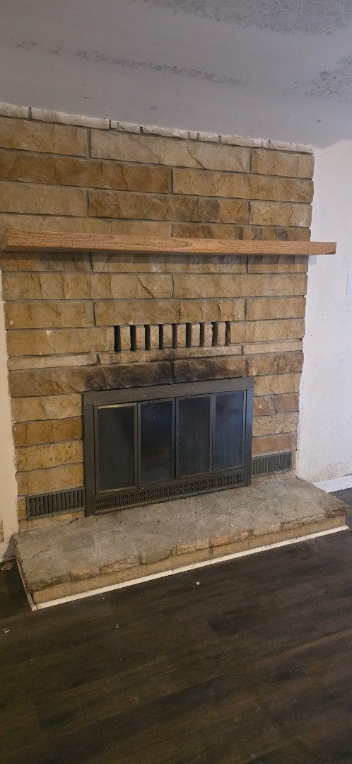 Stone fireplace with dark metal screen, light wood mantel, and dark wood floor.