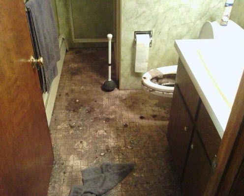 Bathroom with dirty, damaged floor, toilet, plunger, and towel.