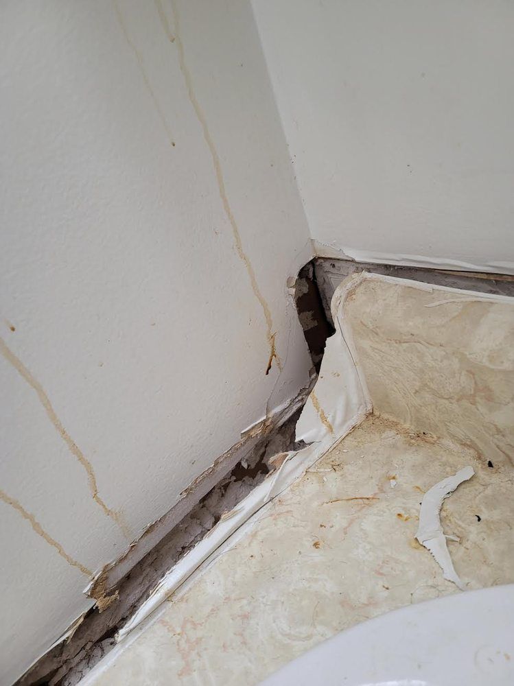 Damaged bathroom wall and ceiling corner with water stains and peeling paint.
