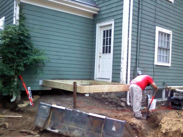 Worker digging beside a green house with a white door during outdoor construction work