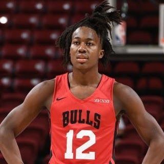 Basketball player in a red Bulls jersey with number 12, hands on hips, looking forward.