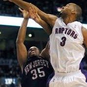 Basketball players in mid-air, one in a Raptors jersey, the other in a New Jersey jersey, contesting a shot.