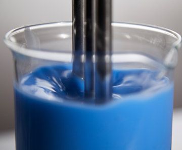 Blue liquid being stirred with a black utensil in a clear plastic cup