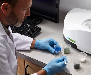Scientist in blue gloves handling samples beside lab equipment at a desk