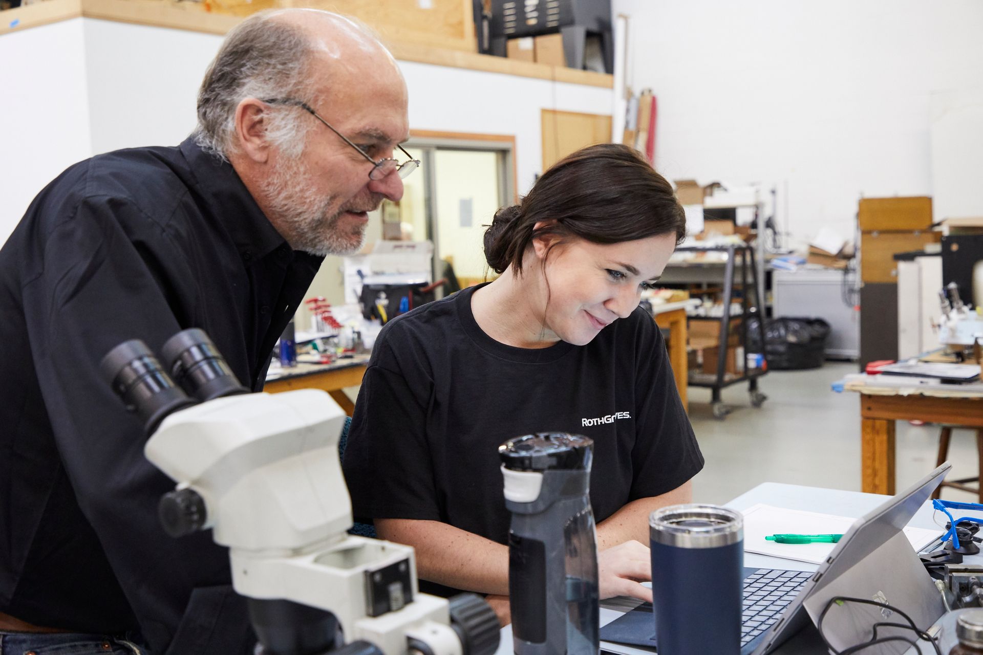 Two people examining a laptop in a lab beside a microscope and equipment.