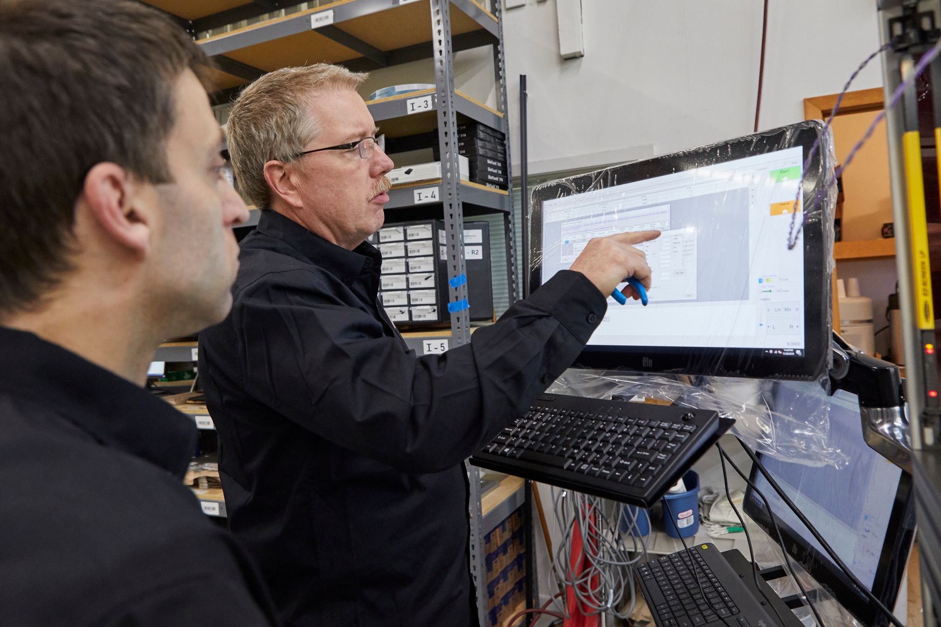 Two technicians inspecting a monitor in a server room, one pointing at the screen.