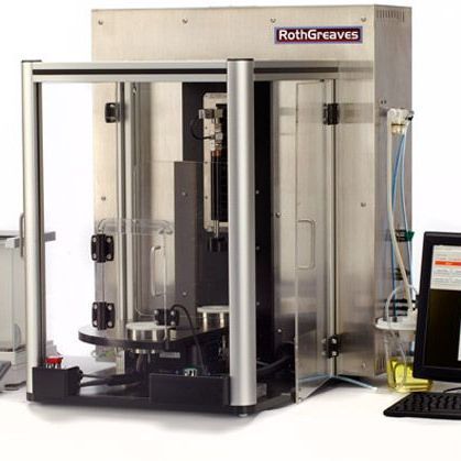 Glass-enclosed industrial machine with RothGreaves logo, clear panels, and control equipment inside lab setting