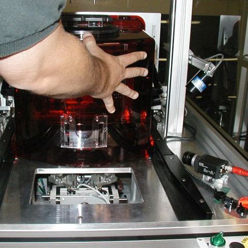 Hand reaching into a red-lit machine inside a metal enclosure on a workbench