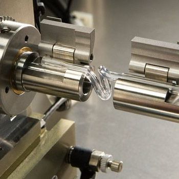 Close-up of a lathe machining a clear, curled plastic ribbon between two metal chucks