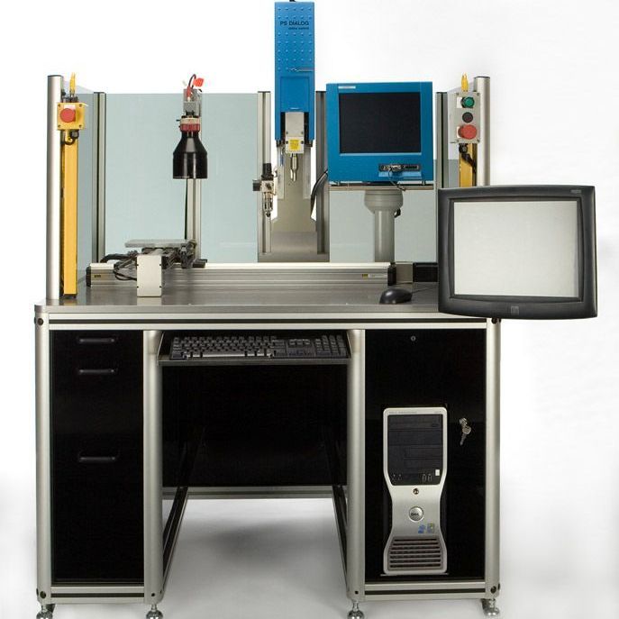 Industrial workstation with dual monitors, control panels, and a computer tower on a black desk