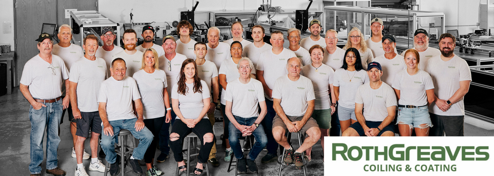 Group of people in white shirts posing in a bright industrial workshop with the RothGreaves logo at bottom right