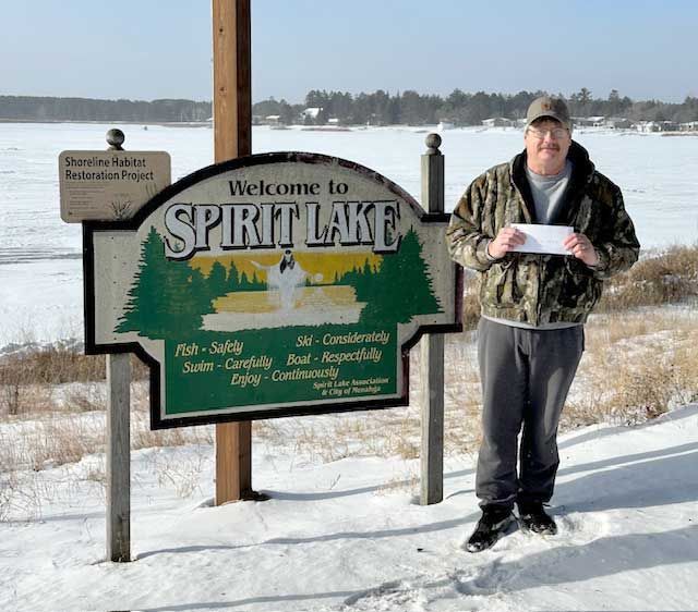 A person in camouflage clothing stands in the snow beside a sign that says