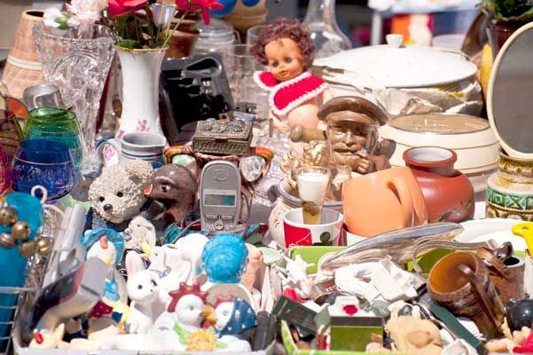 A variety of vintage items and trinkets, including a doll, a glass vase, and a small speaker, arranged at a flea market.