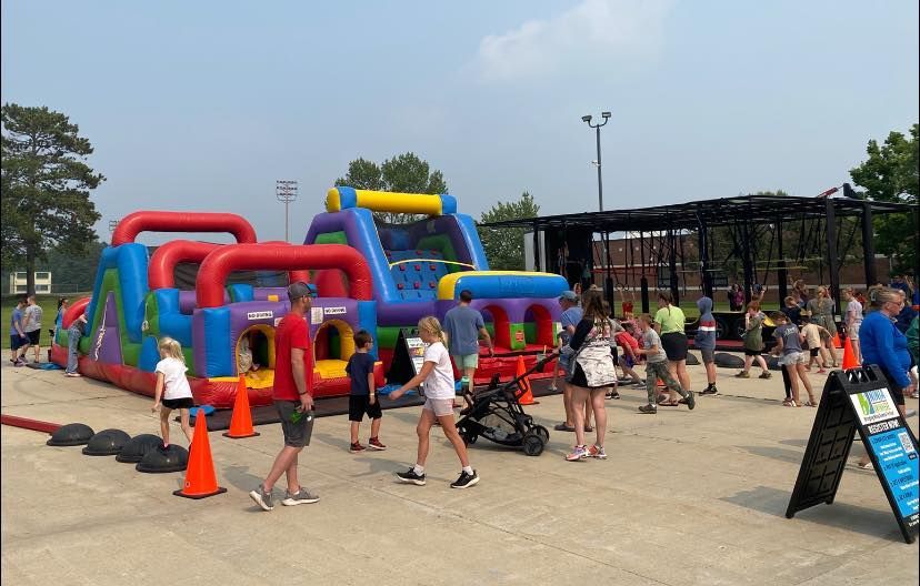 People playing on a colorful inflatable obstacle course at an outdoor park with spectators nearby
