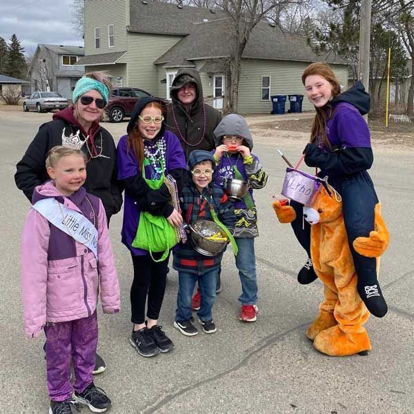 A group of people in winter clothes and costumes standing outdoors, one person wearing an orange bear suit.