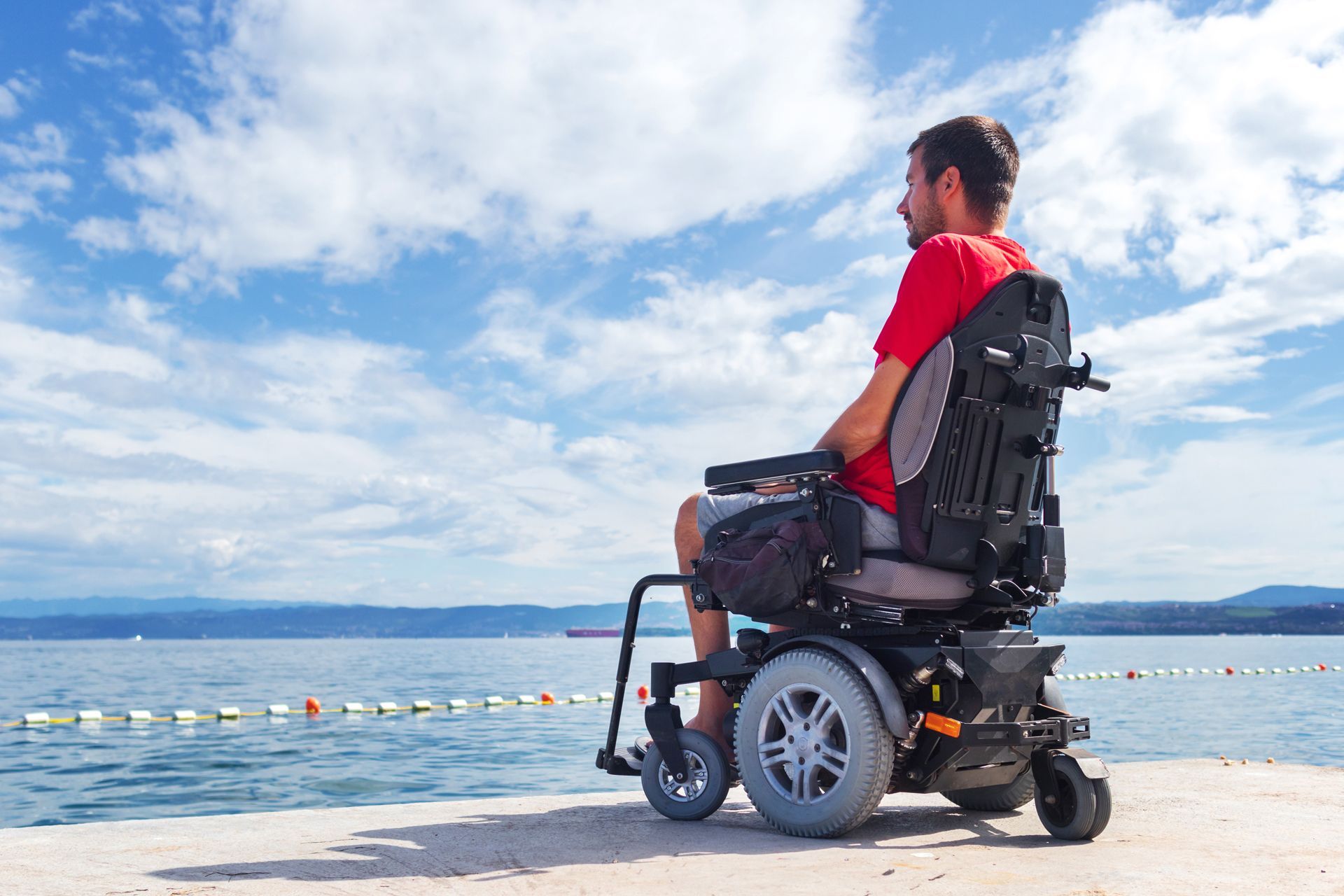 A Man in a Wheelchair is Sitting on the Beach Looking at the Ocean