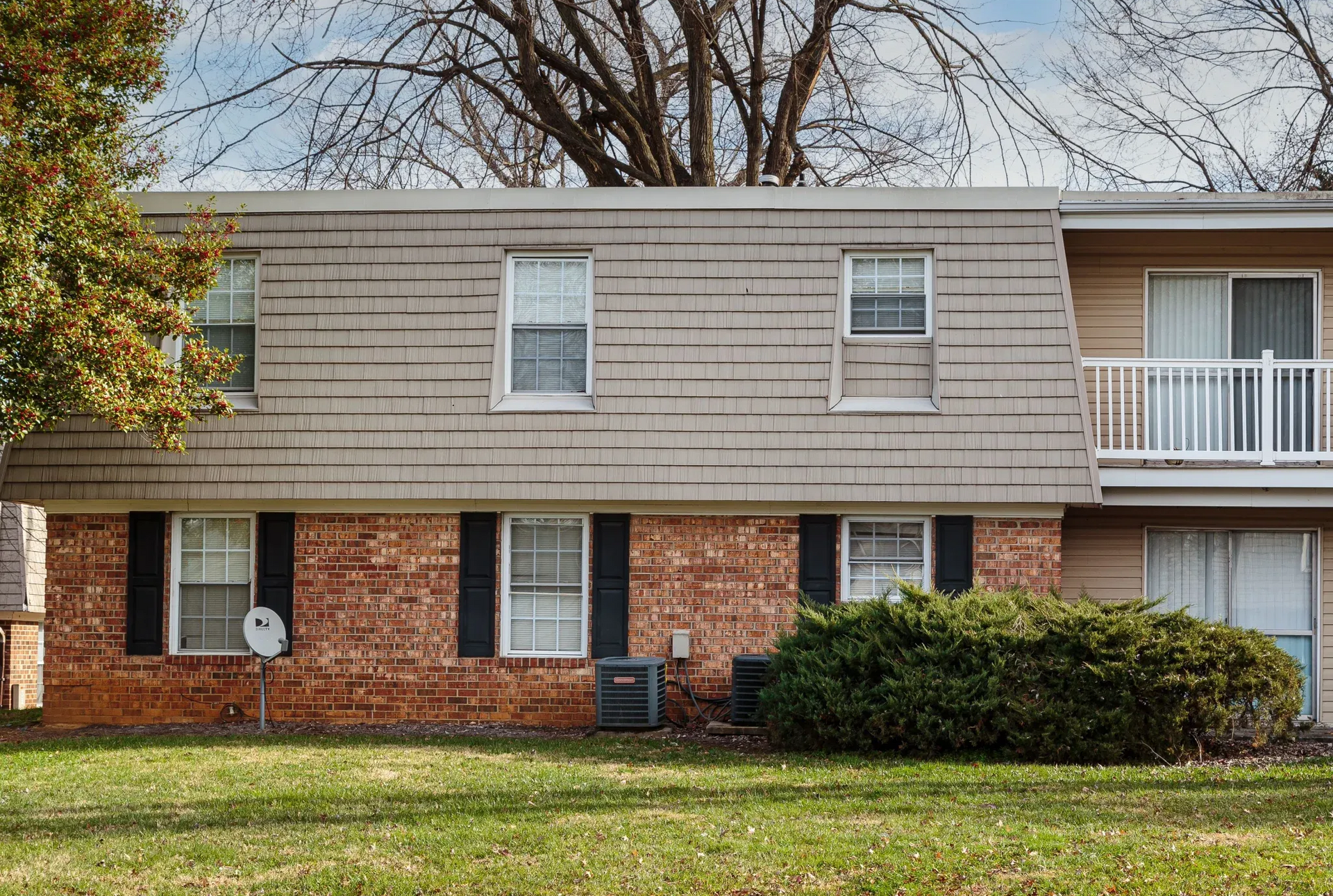 Exterior of a two-story brick-and-beige apartment building with windows and landscaping.