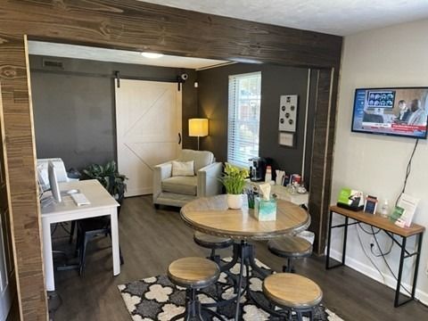 Interior of community office space living area with a round dining table and stools, a sofa, and a wall-mounted TV.