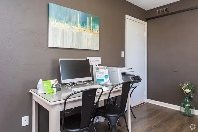 A small workspace with a desk, computer, and printer, against a gray wall, with art at New Irving Heights, which offers apartments near downtown Greensboro, NC.