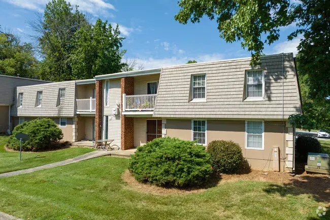 Two-story tan apartment building with a sloped roof and small balconies at New Irving Heights, which offers apartments for rent in Greensboro, NC. Sunny day with green grass and bushes.