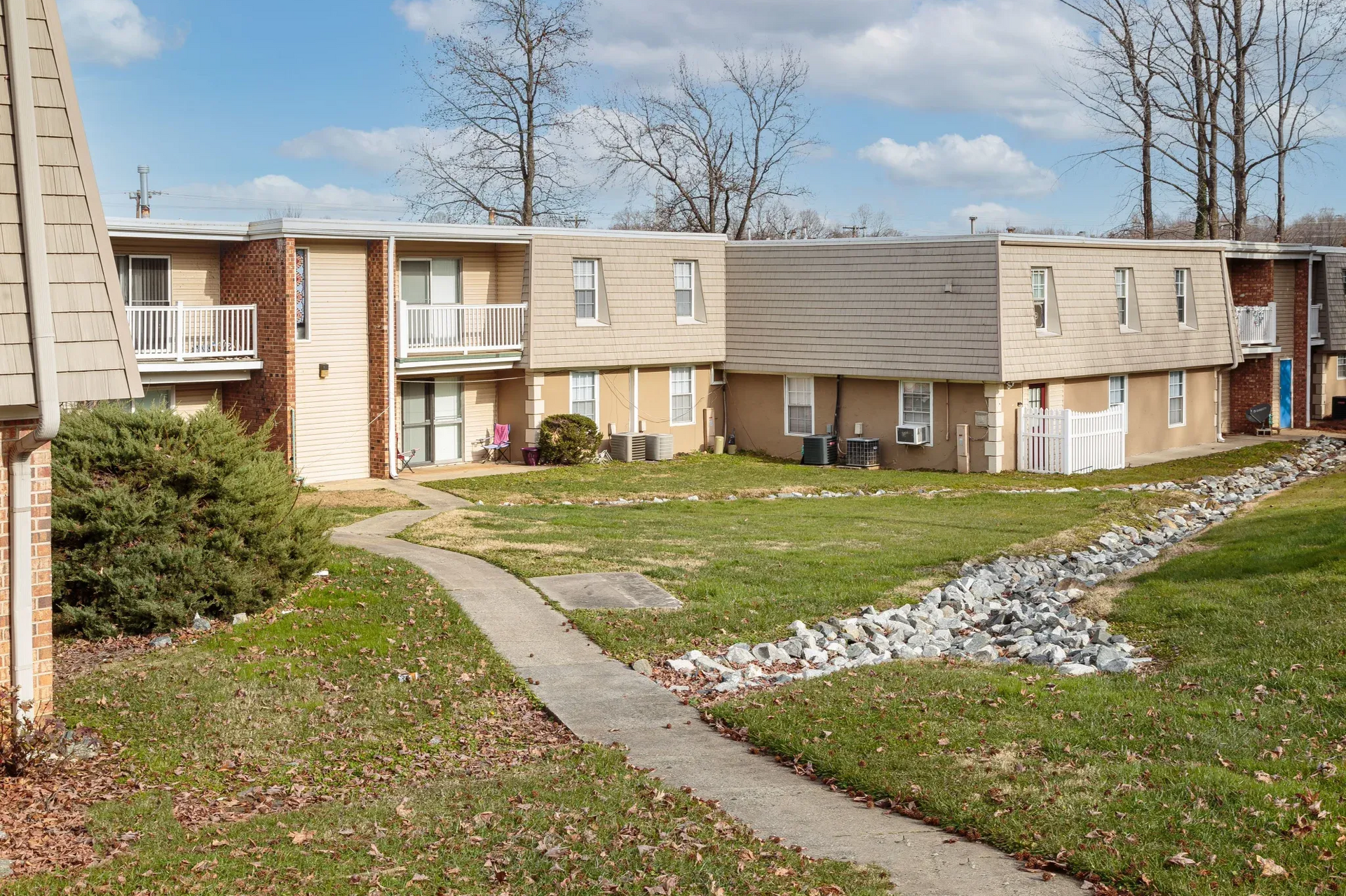Exterior view of a beige two-story apartment complex with walkway and landscaping.