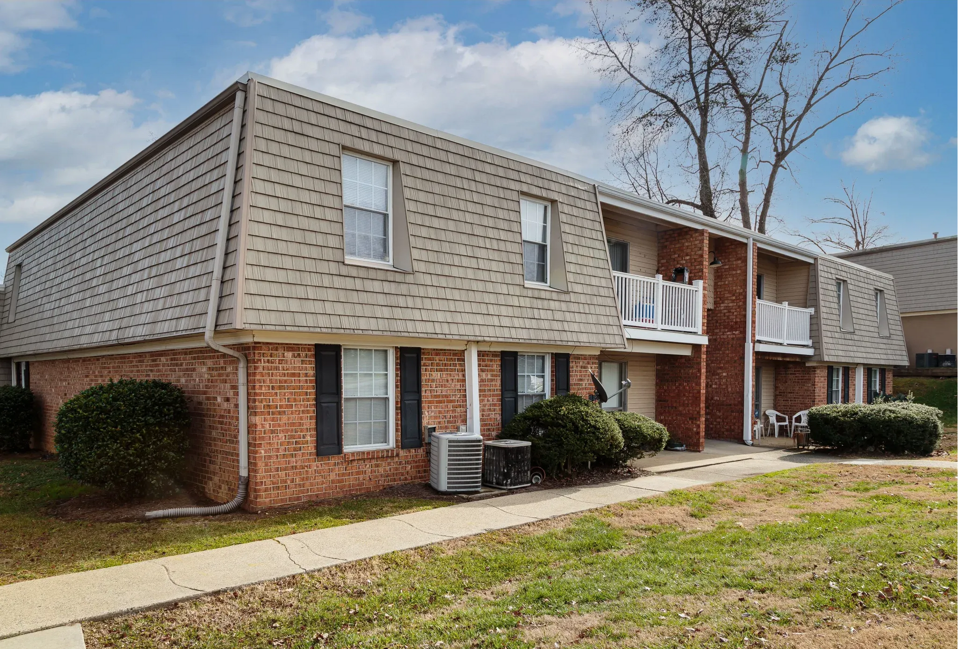 Exterior view of a brick apartment building with a shingled roof and balconies along a walkway.