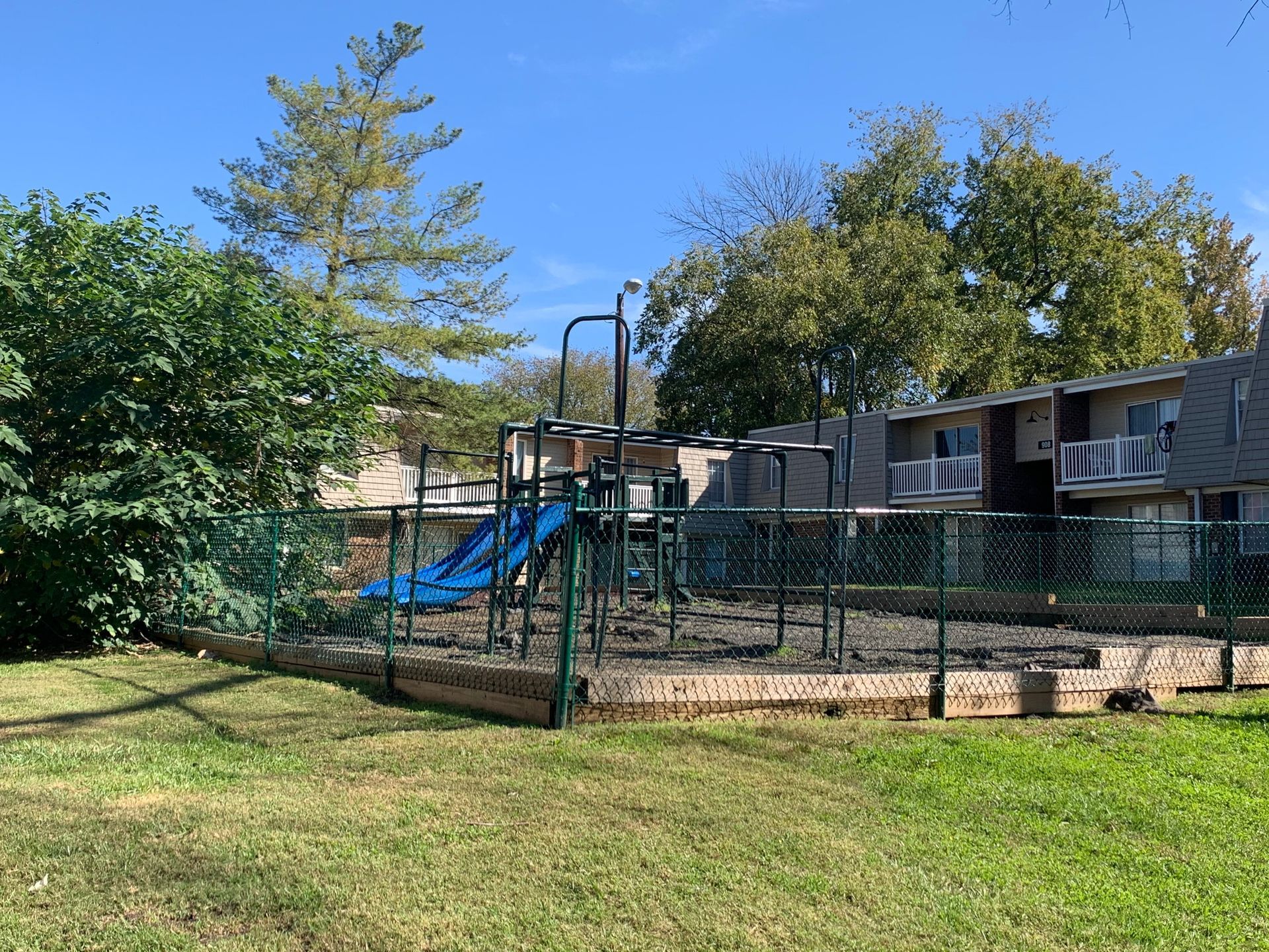 Playground with blue slide and climbing structure inside a fenced yard on a sunny day.