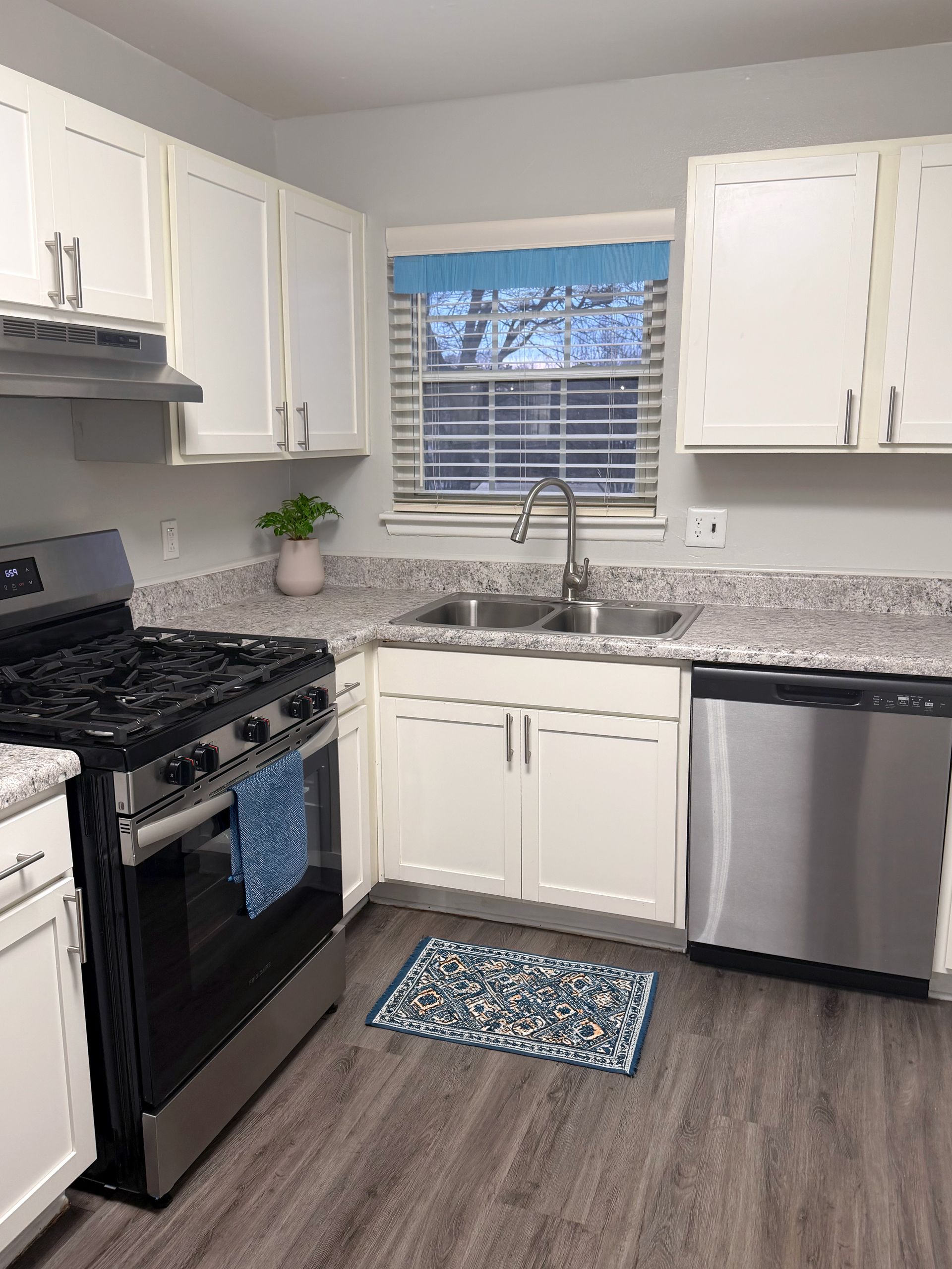 Bright modern kitchen with white cabinets, black stove, stainless dishwasher, and window over sink.