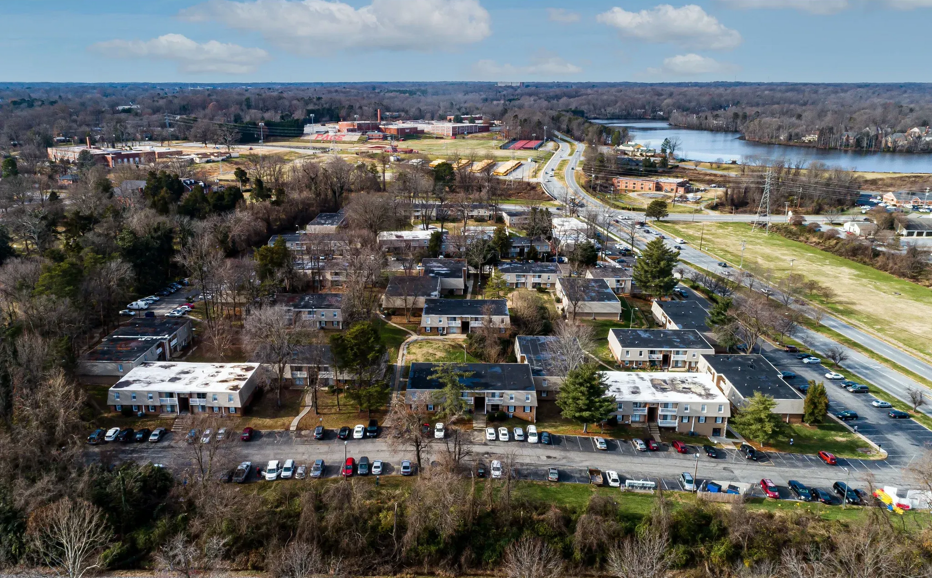 Aerial view of a multifamily apartment community with several buildings, parking lots, and surrounding trees.