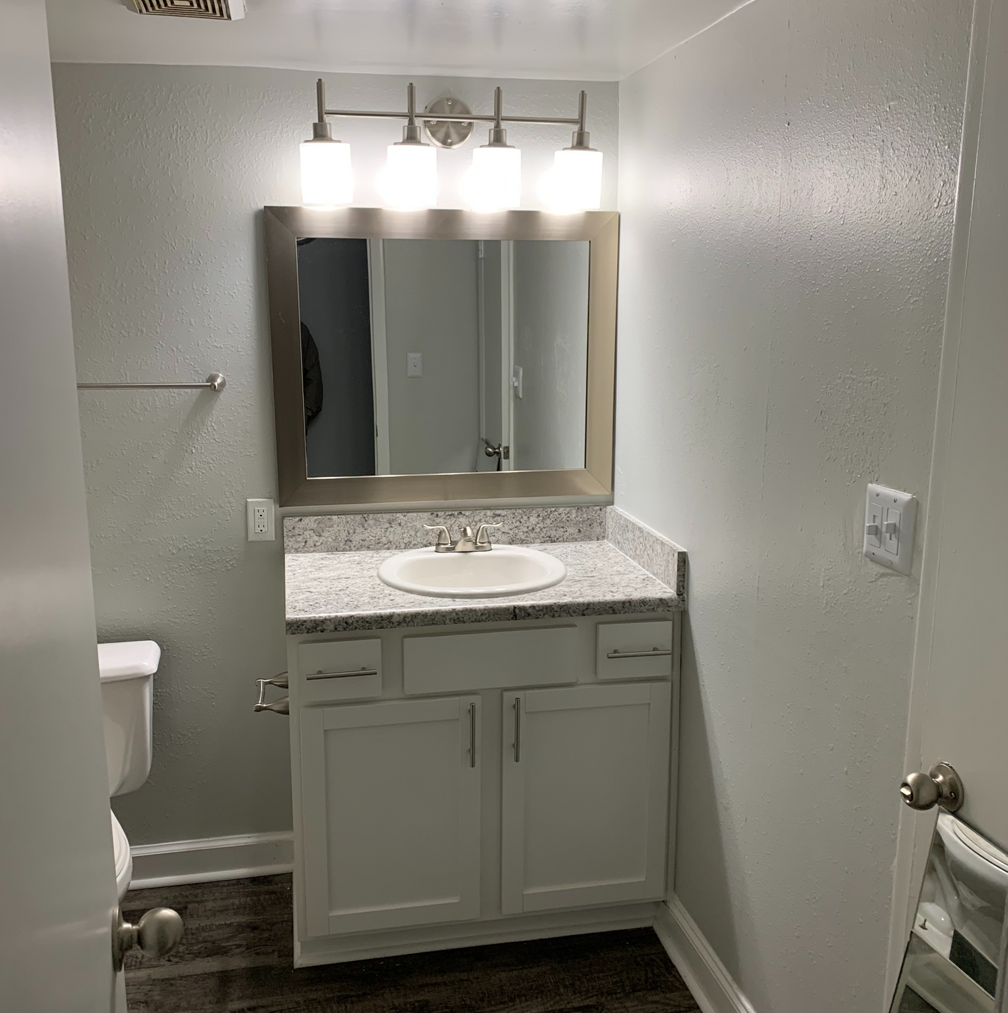 Bathroom vanity with granite countertop, sink, framed mirror, and a four-bulb light fixture.
