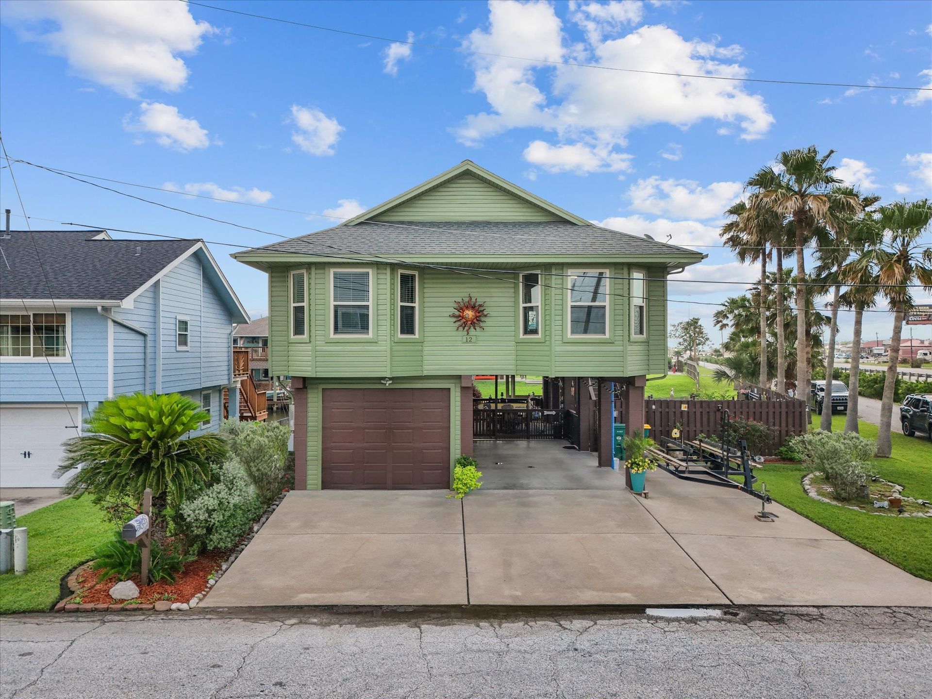 Green beach house on stilts with a brown garage door, and a concrete driveway.