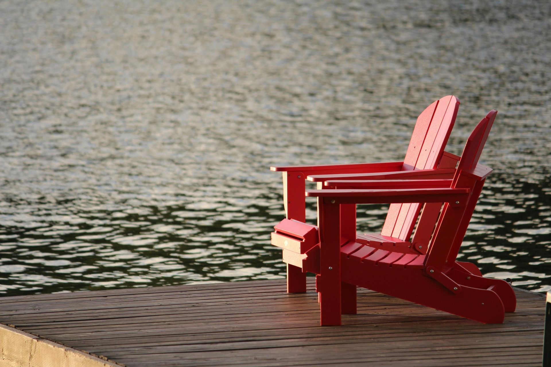 Two red Adirondack chairs on a wooden dock overlooking a body of water.