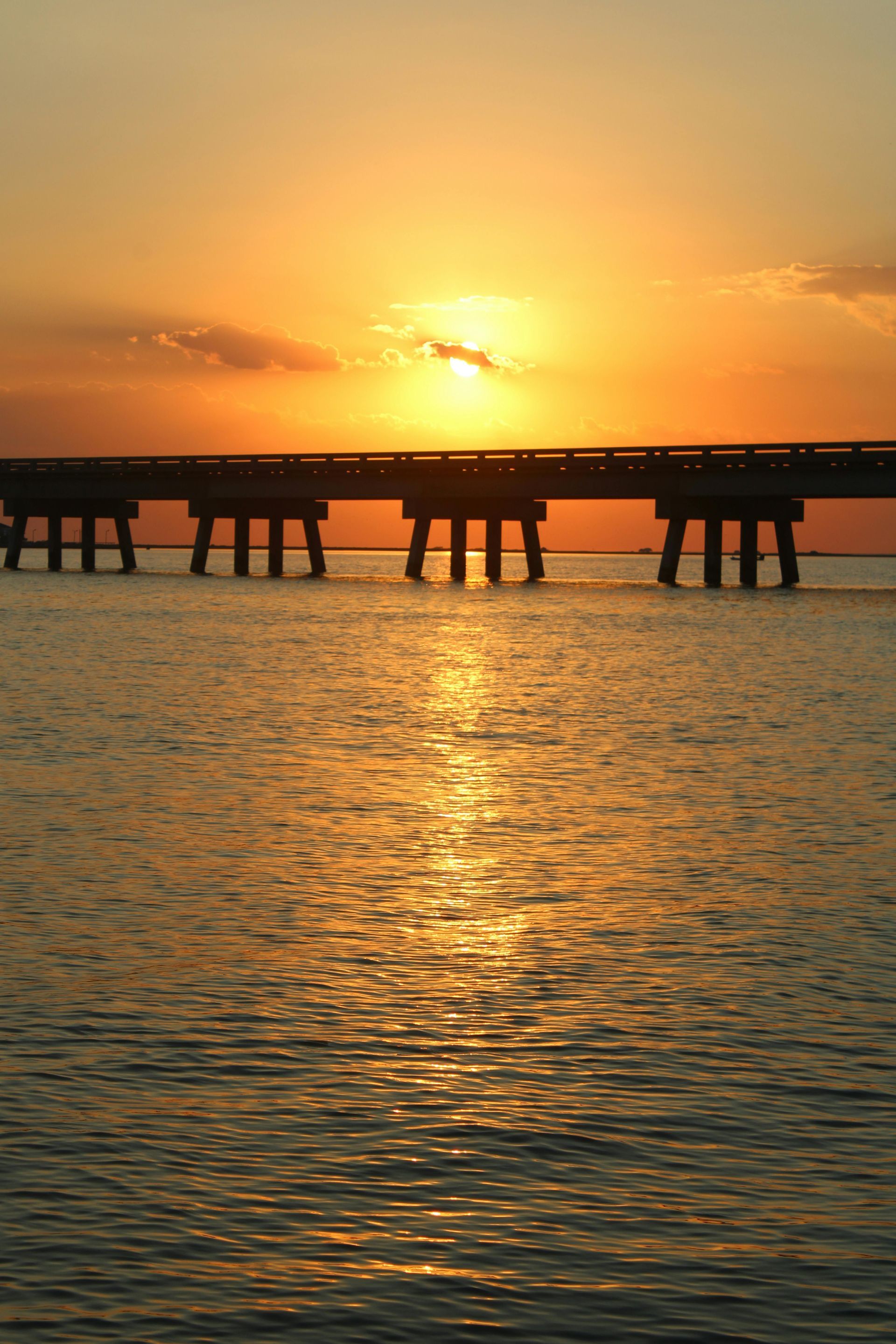 Sunset over a bridge spanning calm water, golden light reflecting.