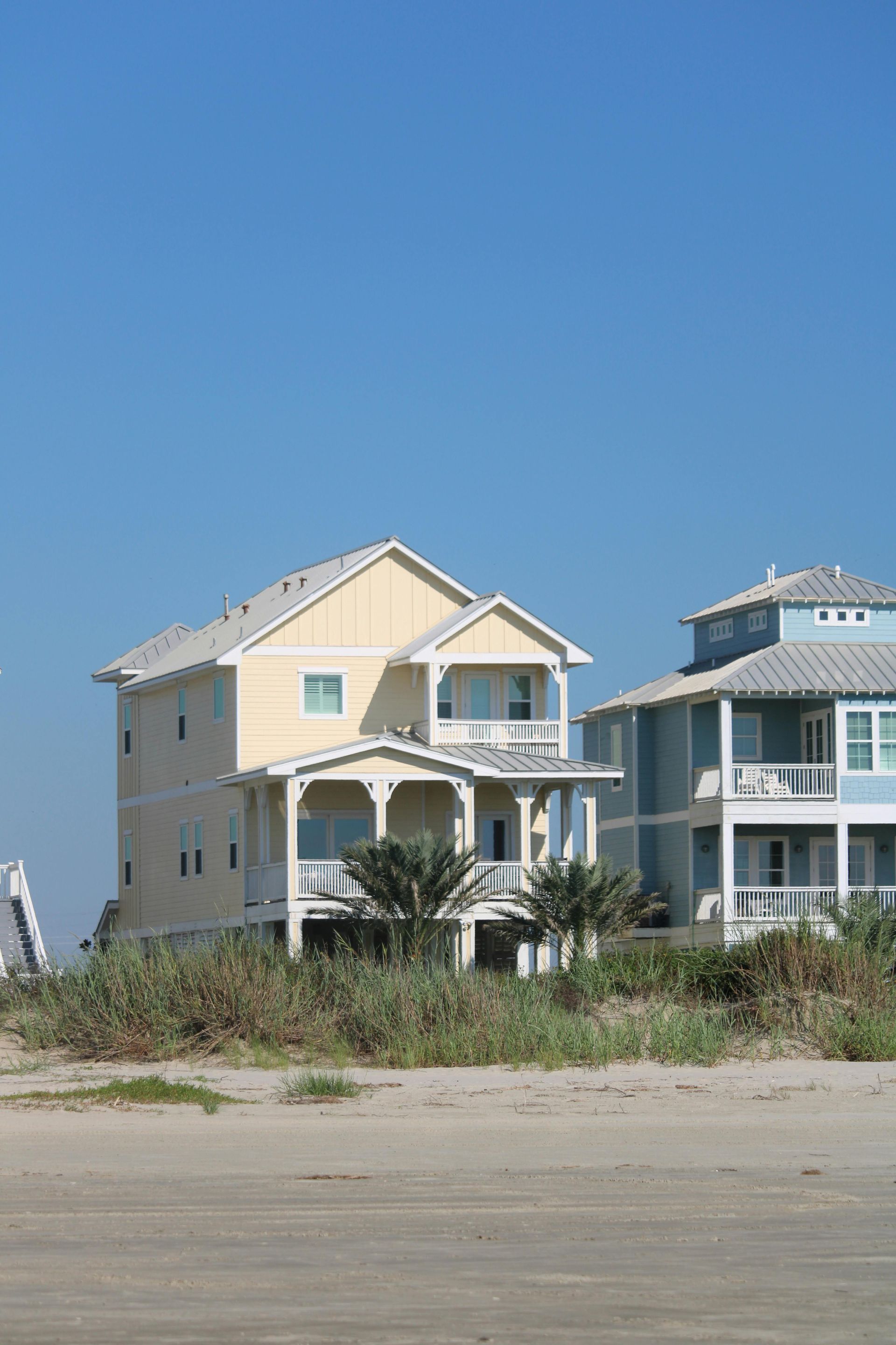 Yellow beach house with balcony beside blue house against clear blue sky.