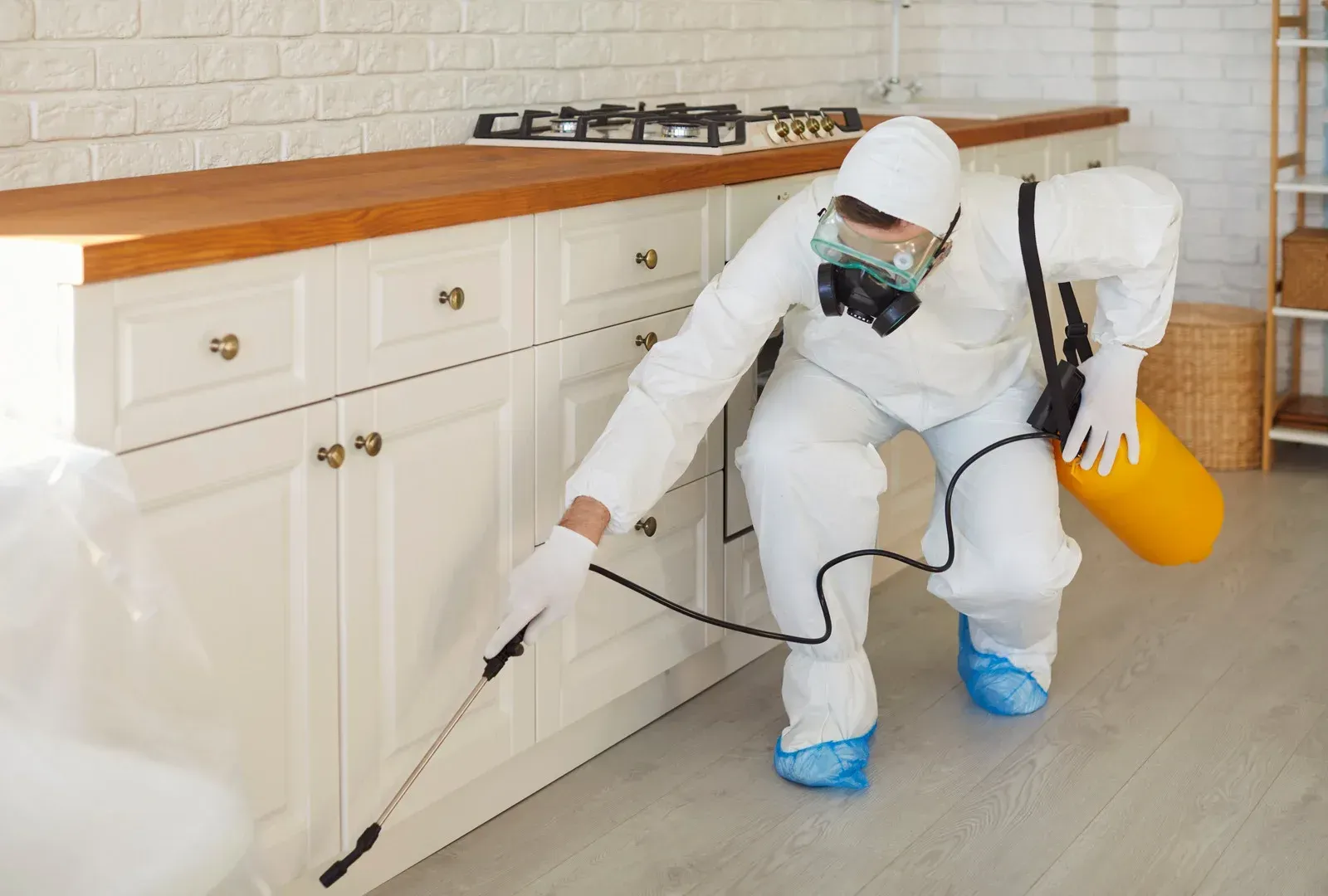 Pest control worker in protective suit sprays insecticide in a kitchen.