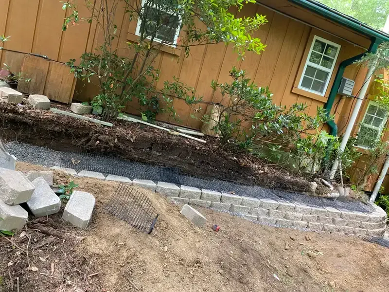 Backyard landscaping with stone border, dirt mound, and orange house exterior.