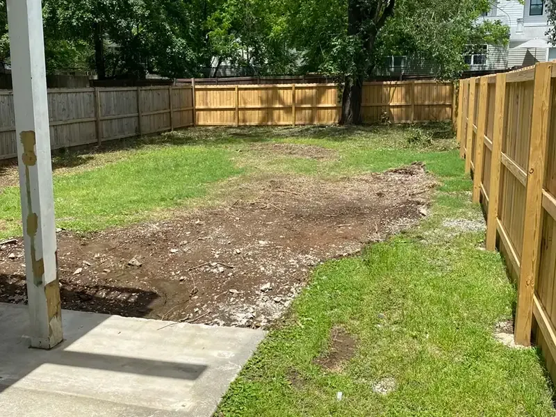 Backyard with a patchy dirt lawn, concrete patio, and wooden fence on three sides