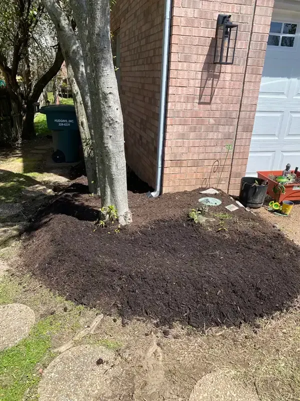 Fresh dark mulch spread in a semicircle around a tree beside a brick house and garage door.
