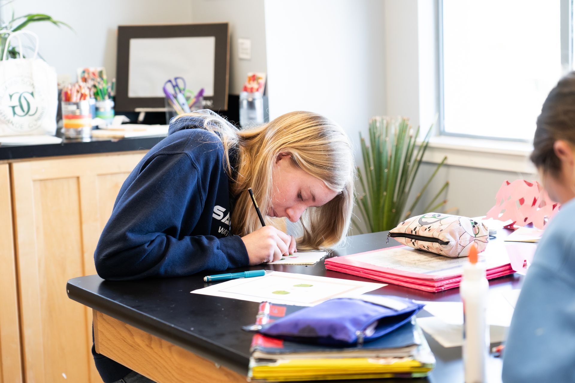 A Montessori child is sitting at a desk in a classroom writing on a piece of paper.