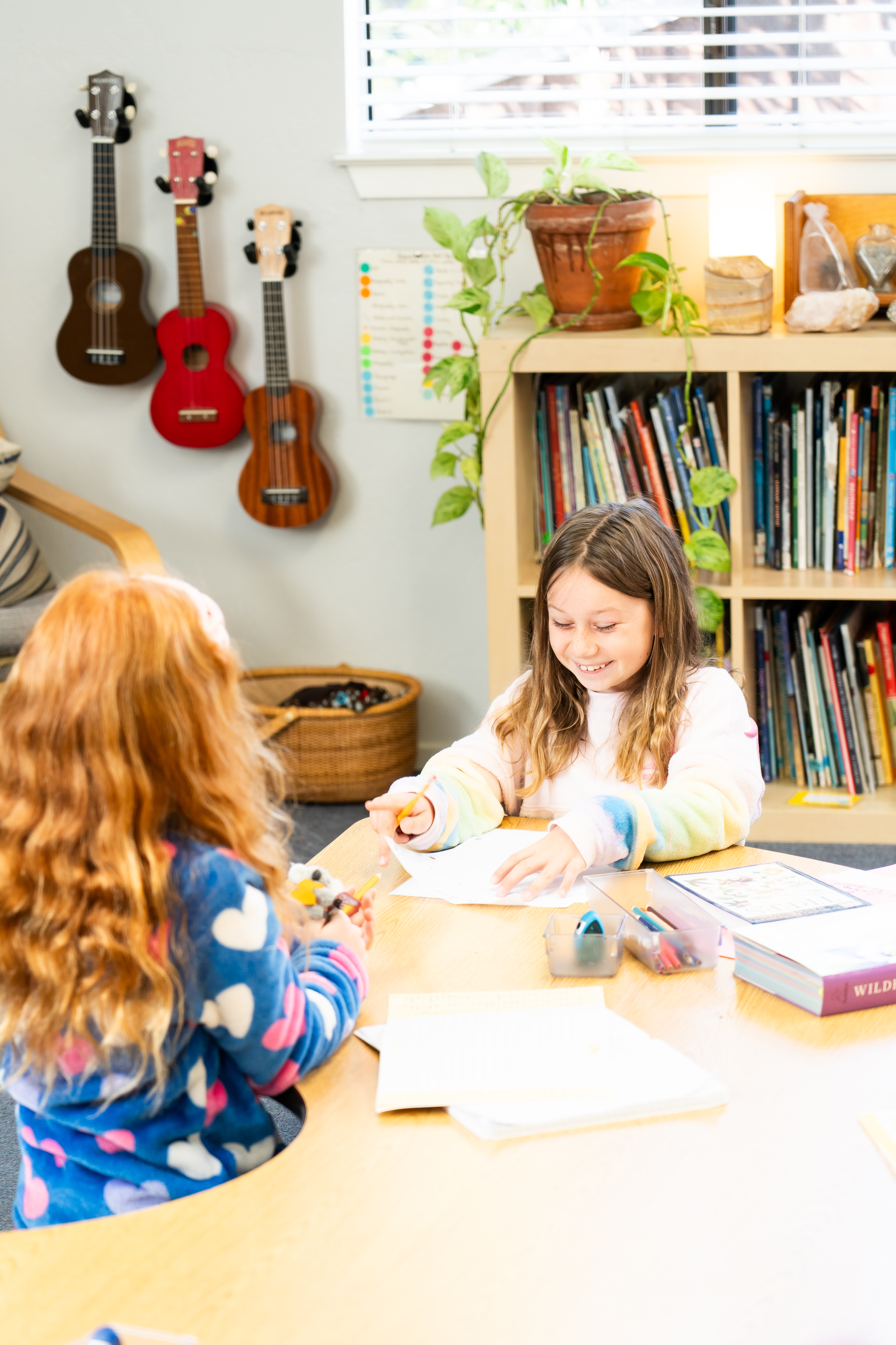 Montessori children are sitting at a table in a room with guitars hanging on the wall.