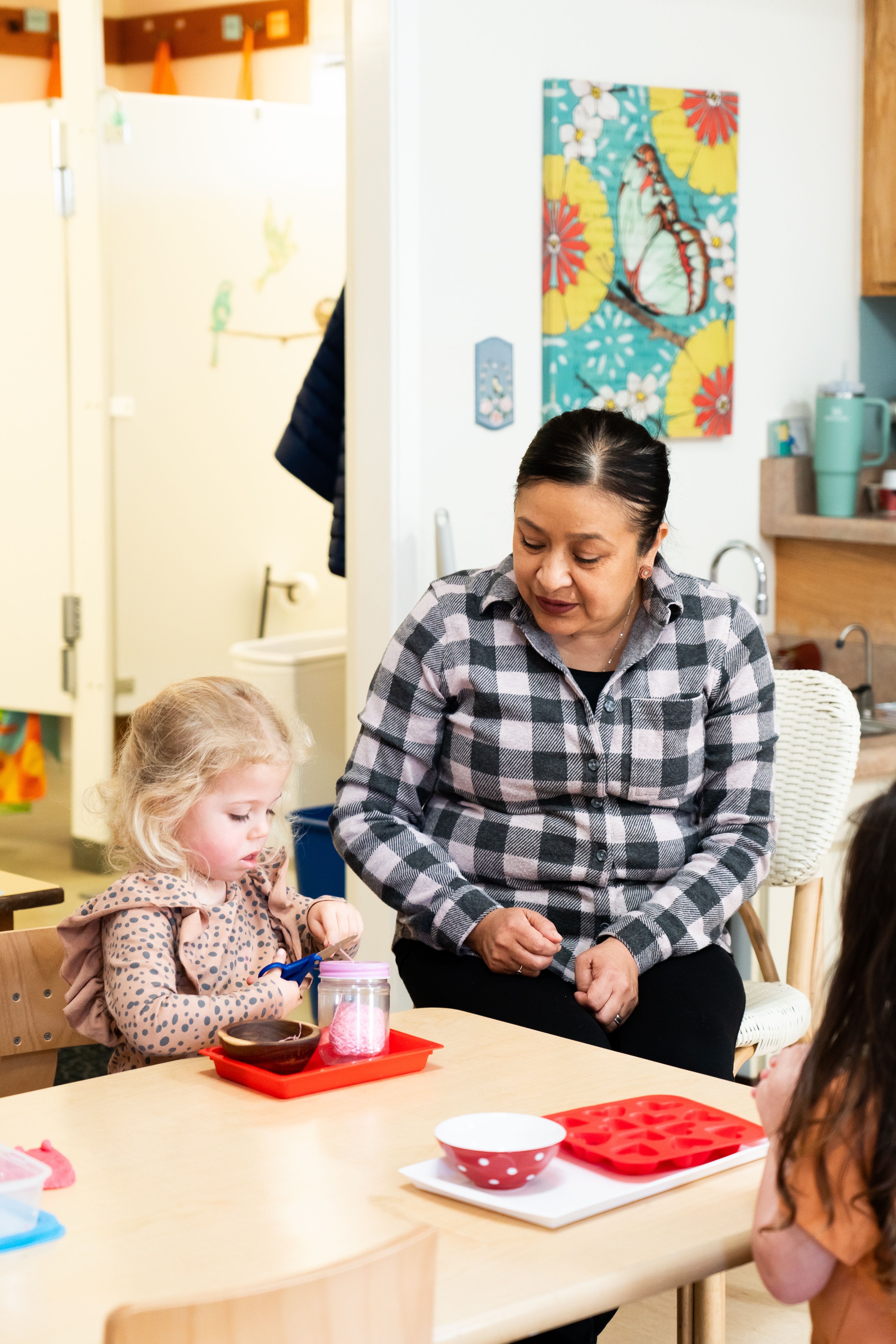 A Montessori guide is sitting at a table with a little girl.