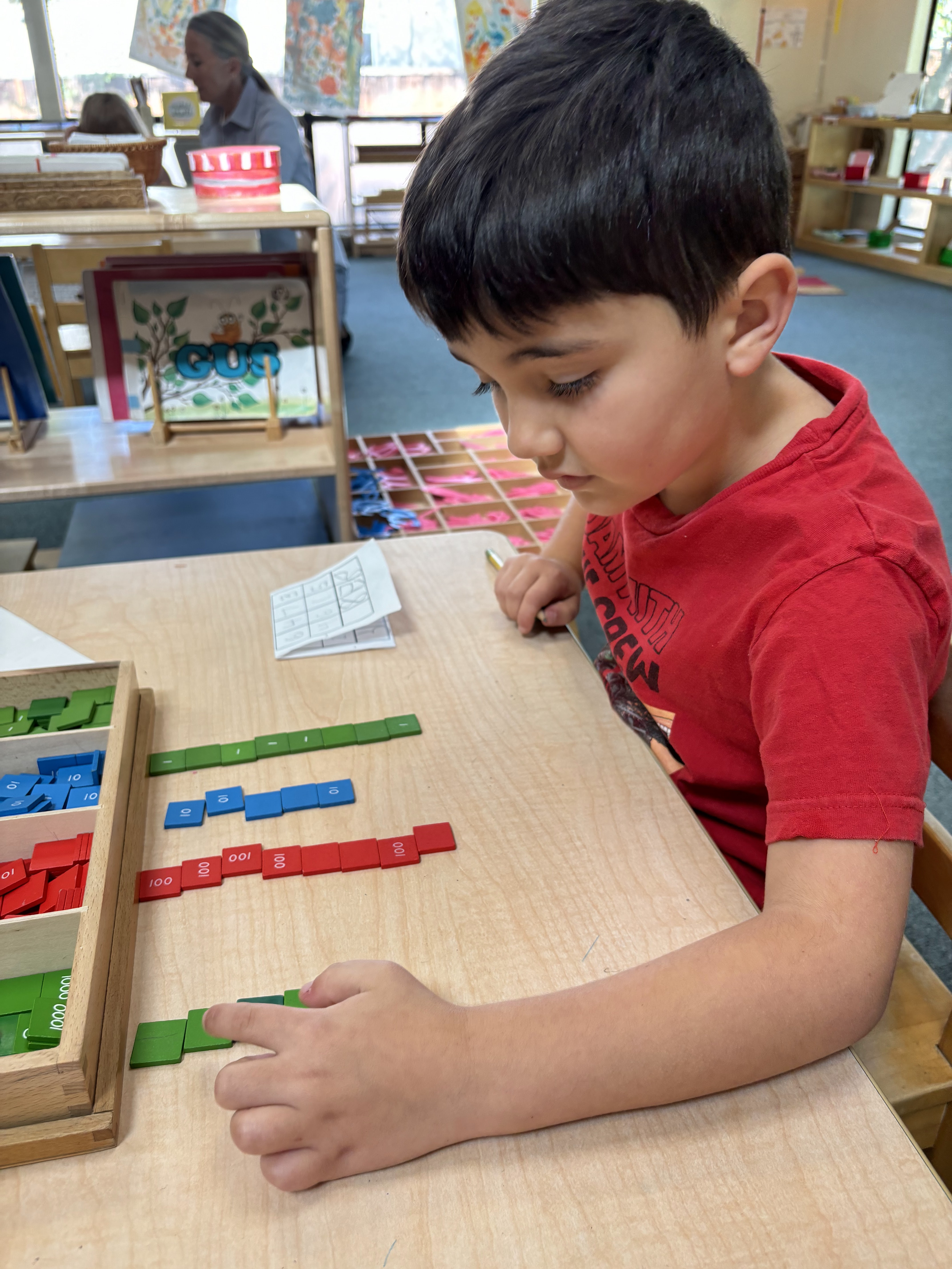 A Montessori child is sitting at a table in a classroom working with toys.
